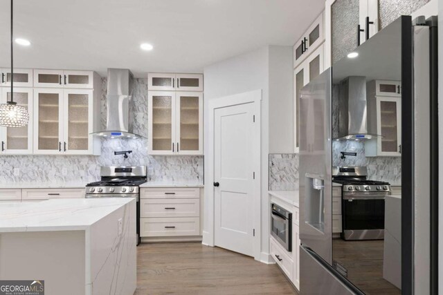 kitchen featuring pendant lighting, wall chimney range hood, backsplash, and appliances with stainless steel finishes