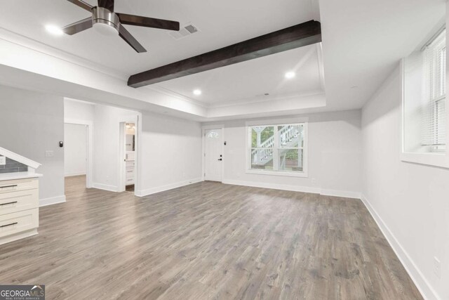 unfurnished living room featuring beamed ceiling, hardwood / wood-style floors, a raised ceiling, and ceiling fan