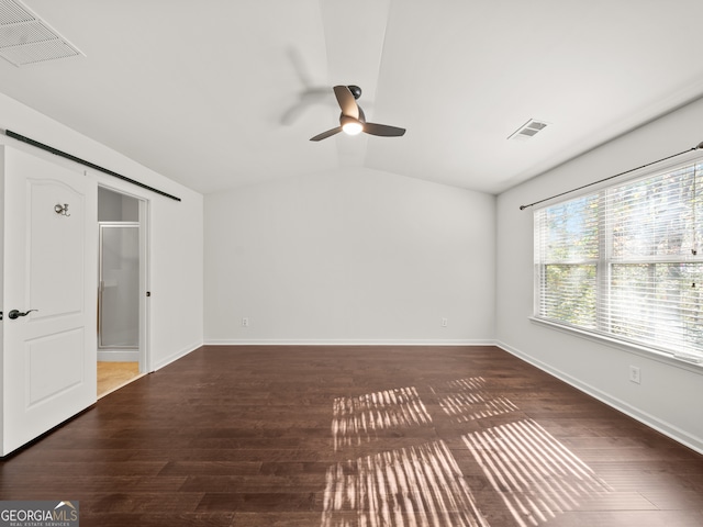 unfurnished room featuring ceiling fan, a barn door, dark hardwood / wood-style flooring, and vaulted ceiling