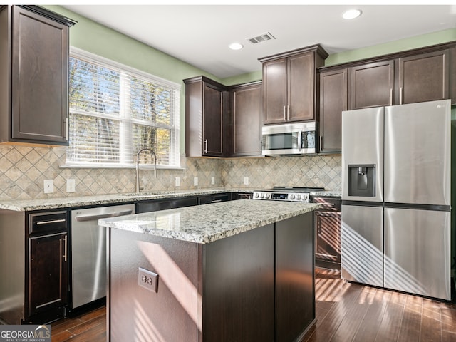 kitchen with sink, dark wood-type flooring, stainless steel appliances, light stone counters, and a kitchen island