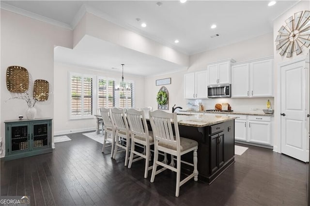 kitchen featuring crown molding, decorative light fixtures, dark hardwood / wood-style floors, white cabinetry, and an island with sink