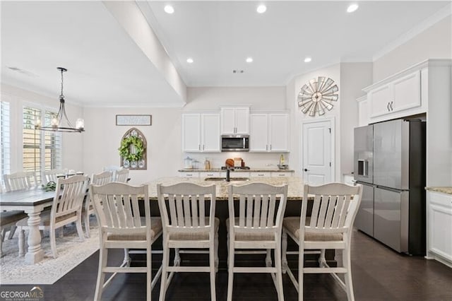 kitchen featuring appliances with stainless steel finishes, light stone counters, a kitchen island with sink, and crown molding