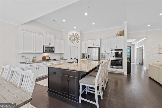 kitchen with light stone countertops, white cabinetry, stainless steel appliances, an island with sink, and a breakfast bar area