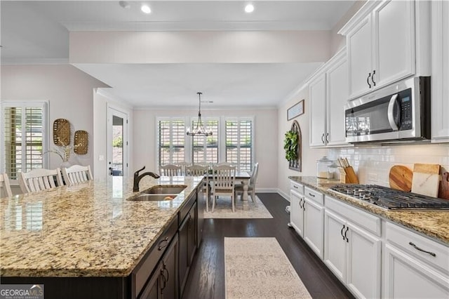 kitchen featuring appliances with stainless steel finishes, sink, decorative light fixtures, white cabinets, and an island with sink