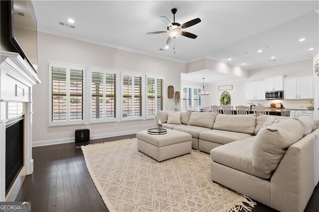 living room featuring hardwood / wood-style floors, a healthy amount of sunlight, ceiling fan with notable chandelier, and ornamental molding