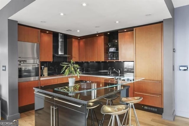 kitchen with light hardwood / wood-style floors, wall chimney range hood, stainless steel appliances, and tasteful backsplash