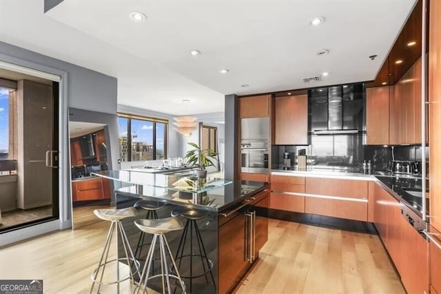 kitchen with a center island, a kitchen breakfast bar, tasteful backsplash, decorative light fixtures, and light hardwood / wood-style floors