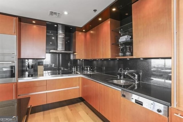 kitchen with decorative backsplash, stainless steel appliances, wall chimney range hood, sink, and light hardwood / wood-style flooring