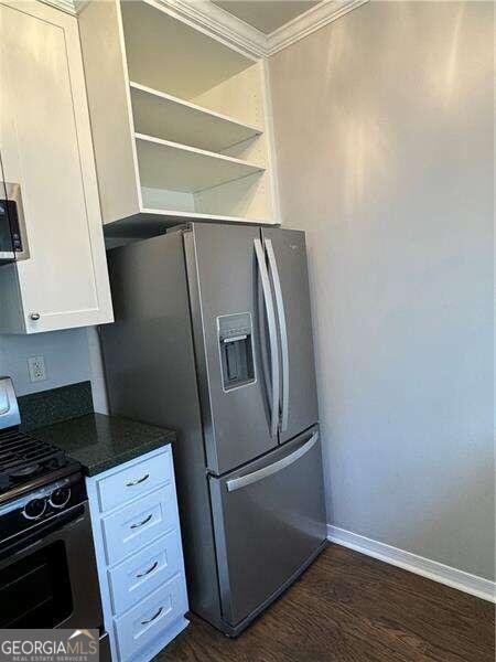 kitchen with white cabinets, dark hardwood / wood-style flooring, ornamental molding, and appliances with stainless steel finishes