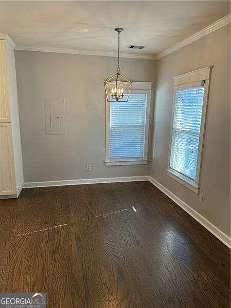 unfurnished dining area featuring dark hardwood / wood-style flooring, crown molding, and an inviting chandelier