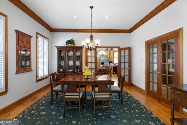 dining room with a chandelier, wood-type flooring, crown molding, and french doors