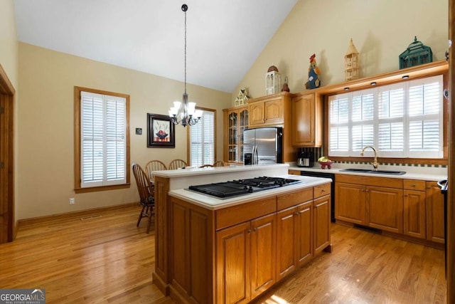 kitchen featuring sink, gas stovetop, light hardwood / wood-style flooring, stainless steel fridge, and decorative light fixtures