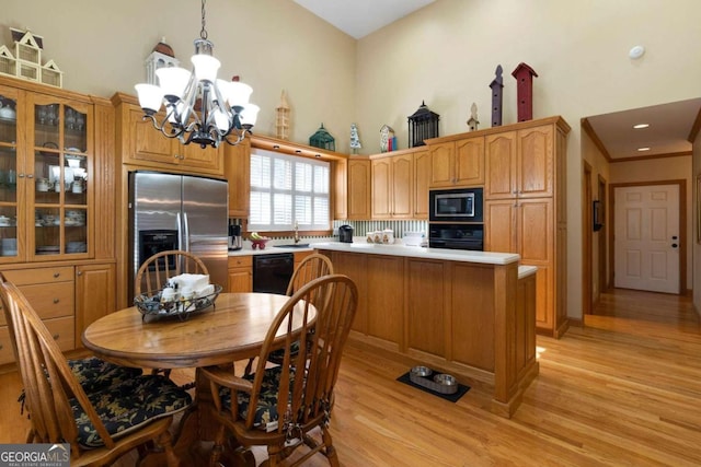 kitchen featuring light wood-type flooring, decorative light fixtures, a notable chandelier, and black appliances