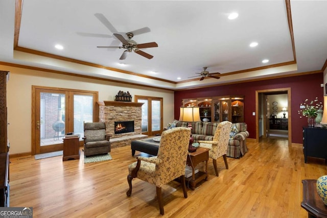 living room featuring french doors, a tray ceiling, ceiling fan, light hardwood / wood-style flooring, and a fireplace