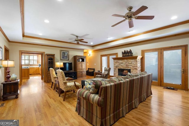 living room featuring ceiling fan, light hardwood / wood-style floors, a stone fireplace, and a tray ceiling