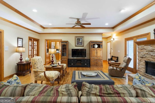 living room with ceiling fan, light hardwood / wood-style floors, a stone fireplace, and ornamental molding