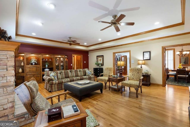 living room featuring a raised ceiling, ornamental molding, ceiling fan with notable chandelier, and light wood-type flooring