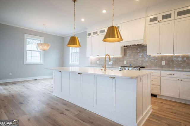 kitchen with crown molding, a center island with sink, decorative light fixtures, and light hardwood / wood-style flooring