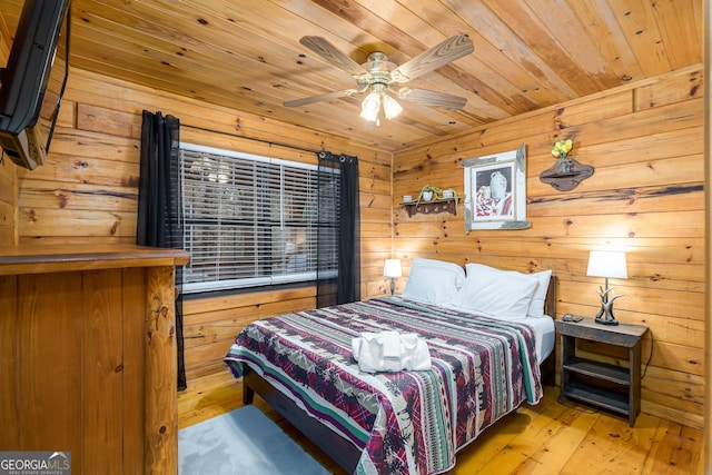 bedroom with ceiling fan, light hardwood / wood-style floors, wood ceiling, and wooden walls