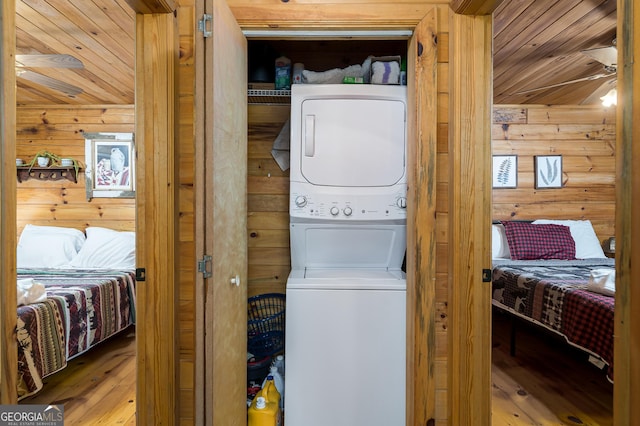 washroom with wooden ceiling, stacked washer and clothes dryer, wood walls, and hardwood / wood-style flooring