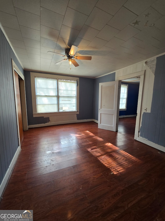 spare room featuring ceiling fan, wooden walls, and dark wood-type flooring