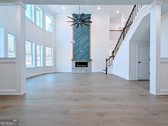 unfurnished living room with a high ceiling, ceiling fan, light wood-type flooring, ornamental molding, and a large fireplace