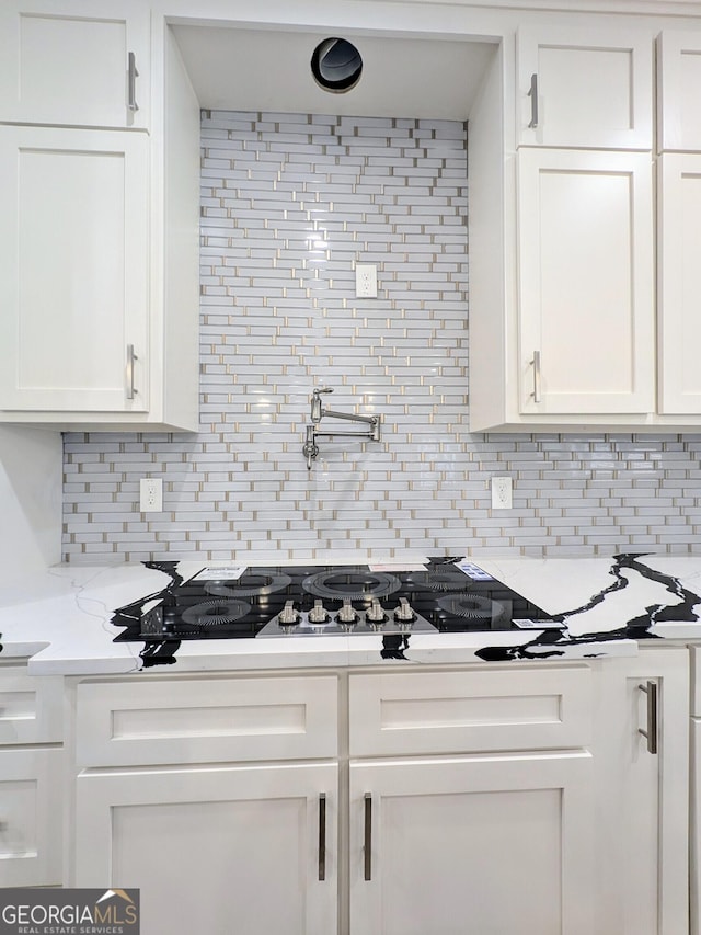 kitchen with tasteful backsplash, light stone countertops, and white cabinets