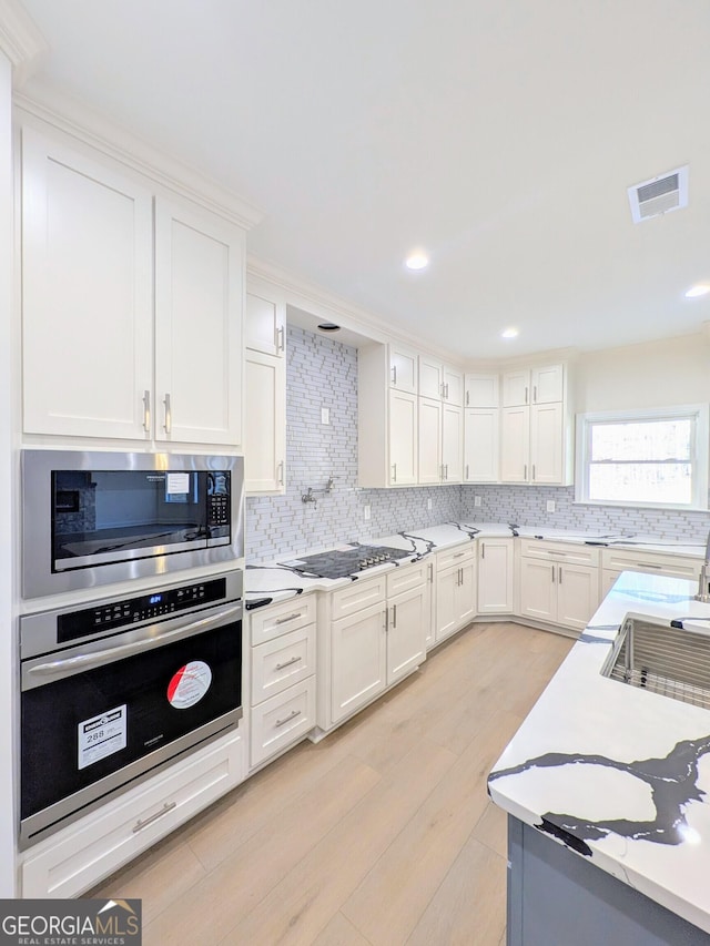 kitchen with decorative backsplash, white cabinetry, light hardwood / wood-style flooring, and appliances with stainless steel finishes