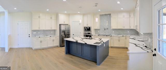 kitchen with a kitchen island with sink, stainless steel appliances, decorative backsplash, white cabinets, and light wood-type flooring