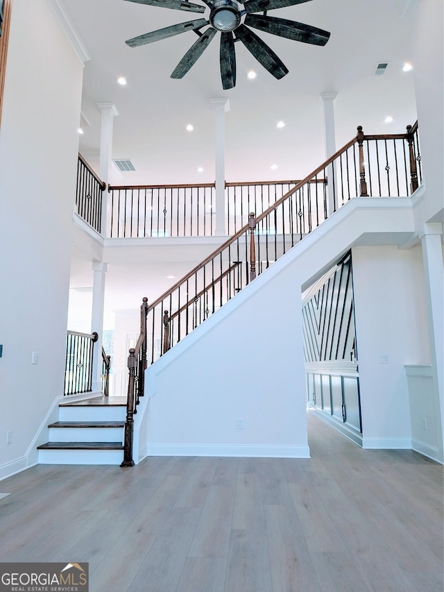 stairs with ornate columns, ceiling fan, a high ceiling, hardwood / wood-style flooring, and ornamental molding