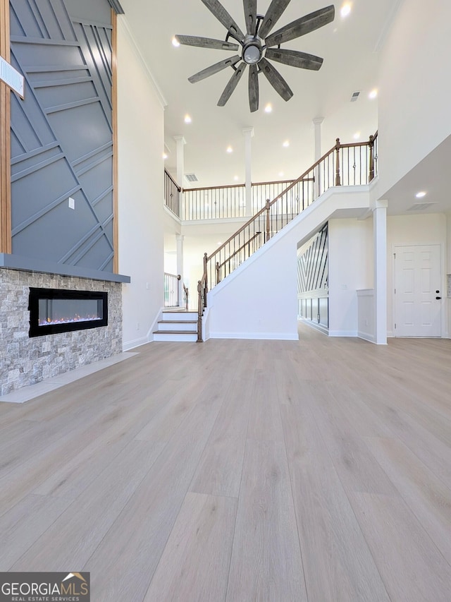 unfurnished living room featuring a stone fireplace, ceiling fan, a high ceiling, and light wood-type flooring