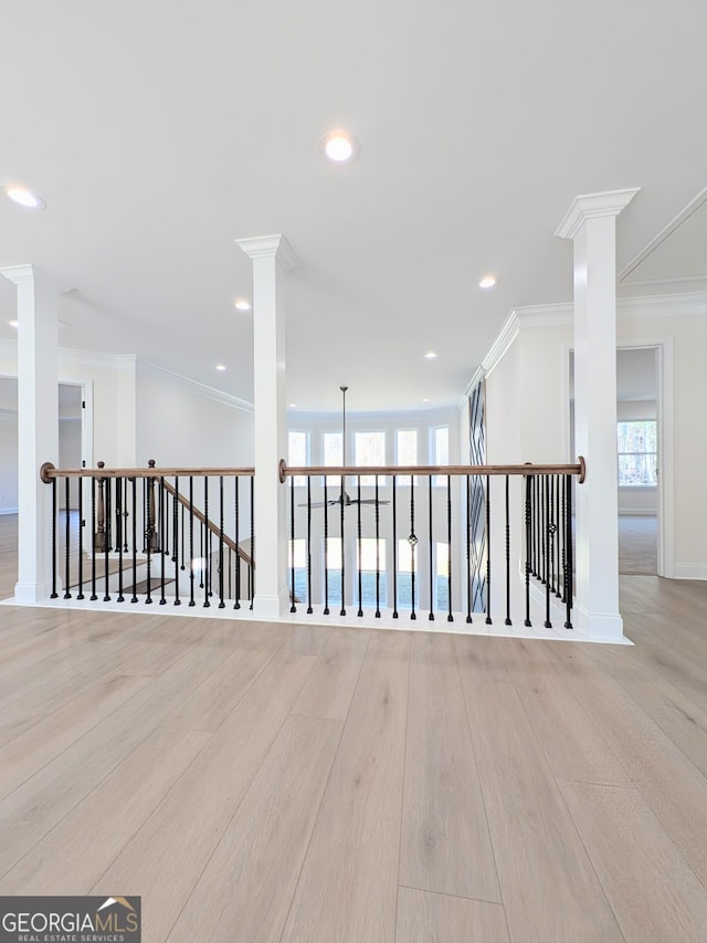 empty room featuring lofted ceiling, light hardwood / wood-style floors, ornamental molding, and decorative columns