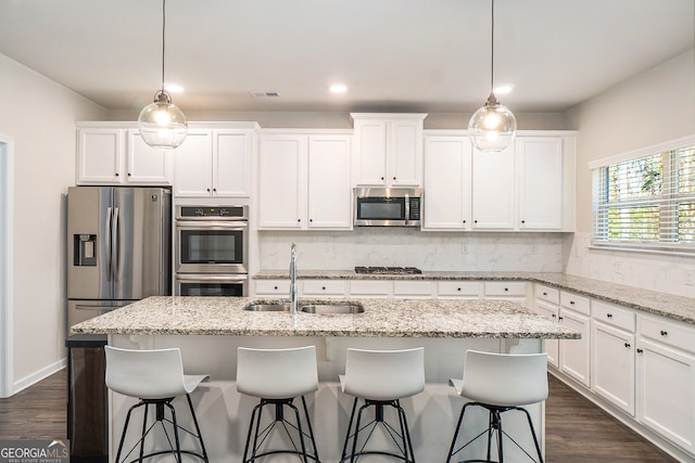 kitchen featuring light stone countertops, appliances with stainless steel finishes, sink, a center island with sink, and white cabinets