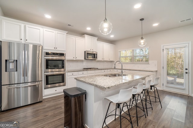 kitchen featuring white cabinetry, sink, stainless steel appliances, a kitchen breakfast bar, and light stone counters