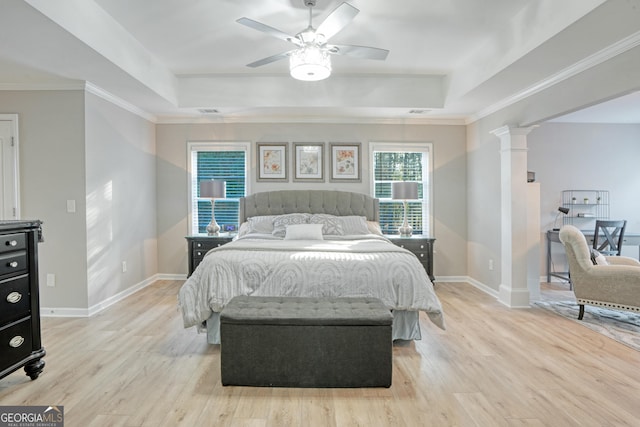 bedroom with ceiling fan, light hardwood / wood-style flooring, decorative columns, a tray ceiling, and ornamental molding