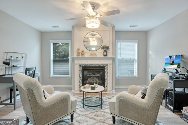 living room with ceiling fan, a premium fireplace, and light hardwood / wood-style flooring