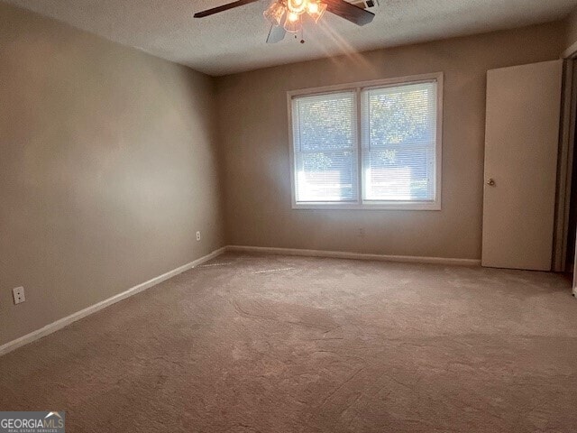 spare room with a textured ceiling, light colored carpet, and ceiling fan