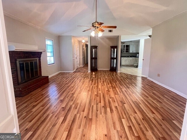 unfurnished living room featuring ceiling fan, a brick fireplace, crown molding, lofted ceiling, and hardwood / wood-style flooring