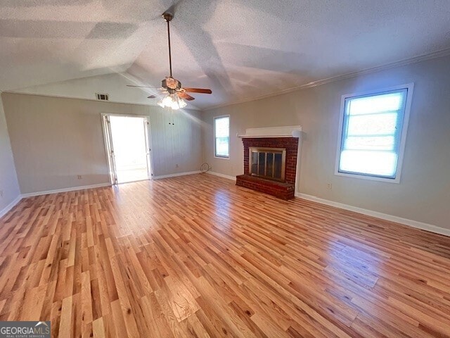 unfurnished living room with ornamental molding, vaulted ceiling, ceiling fan, light hardwood / wood-style flooring, and a fireplace