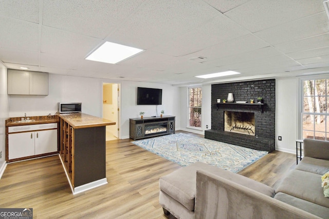 living room featuring light hardwood / wood-style flooring, sink, a paneled ceiling, and a fireplace