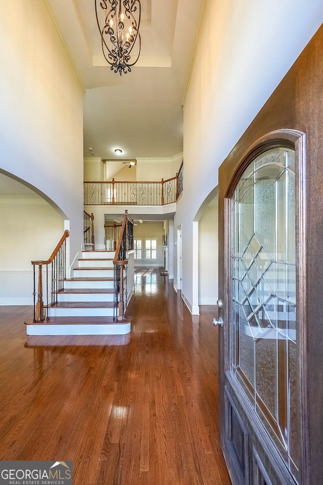 entrance foyer with an inviting chandelier, crown molding, a towering ceiling, a tray ceiling, and wood-type flooring