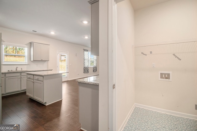 kitchen with light stone countertops, a center island, dark wood-type flooring, tasteful backsplash, and ornamental molding