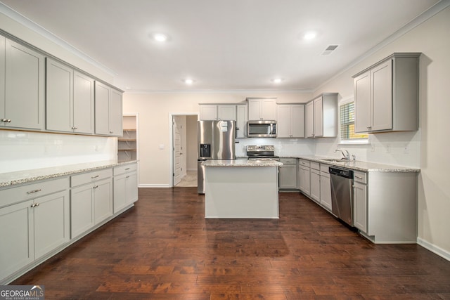 kitchen with sink, light stone countertops, appliances with stainless steel finishes, a kitchen island, and dark hardwood / wood-style flooring