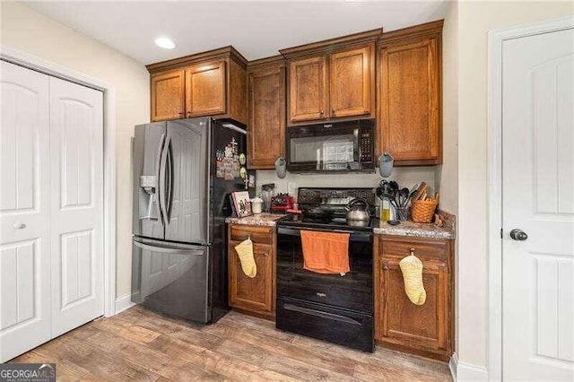 kitchen with light stone countertops, light hardwood / wood-style flooring, and black appliances