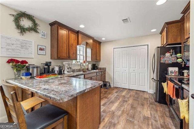 kitchen featuring electric range, sink, dark hardwood / wood-style flooring, kitchen peninsula, and a breakfast bar area