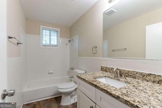 full bathroom featuring tiled shower / bath combo, hardwood / wood-style floors, toilet, vanity, and tile walls