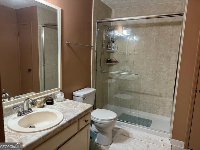 bathroom with vanity, toilet, a shower with shower door, and a textured ceiling