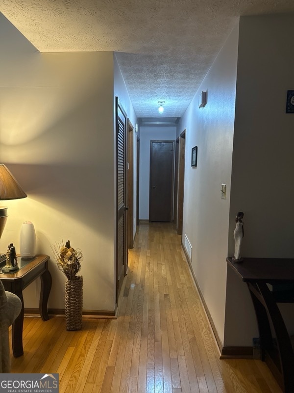 corridor with light wood-type flooring and a textured ceiling