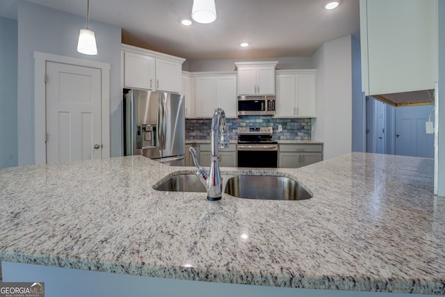 kitchen with sink, light stone counters, decorative light fixtures, white cabinets, and appliances with stainless steel finishes