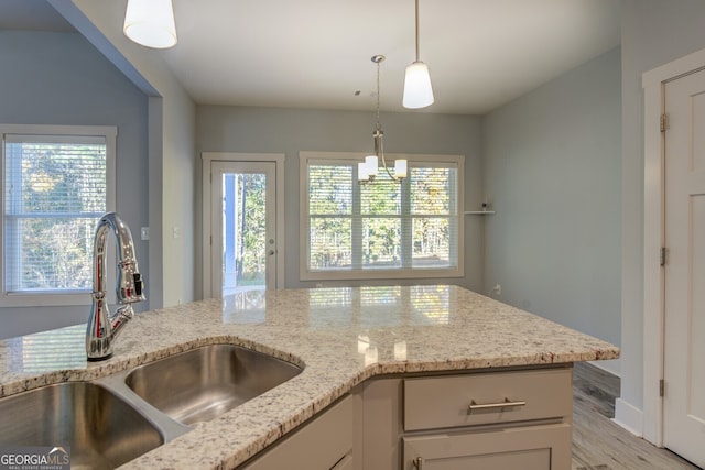 kitchen with light stone countertops, sink, decorative light fixtures, white cabinets, and light wood-type flooring